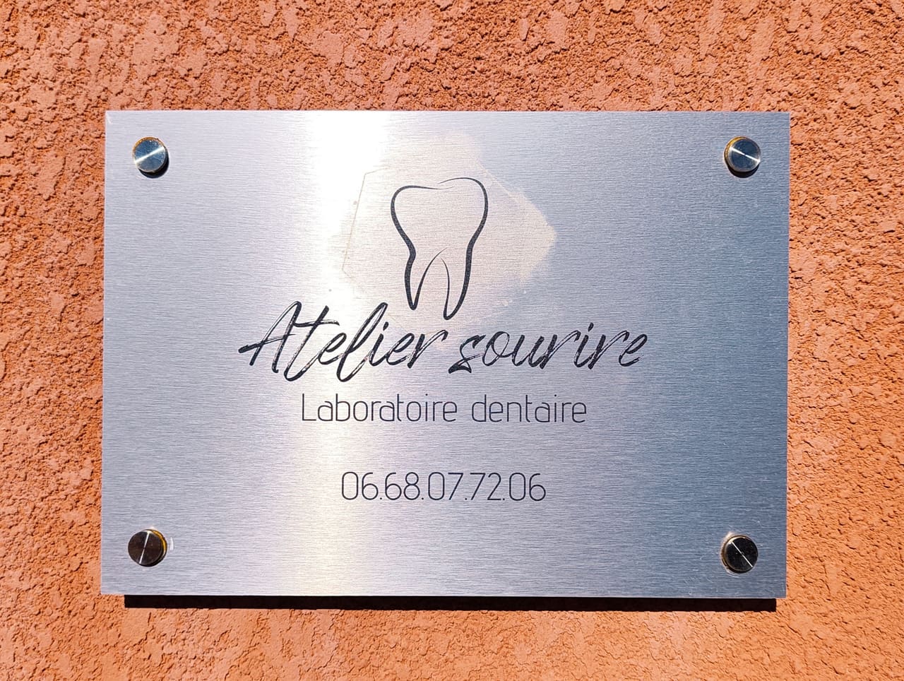 Plaque en inox à l’entrée du laboratoire : Atelier Sourire, laboratoire dentaire